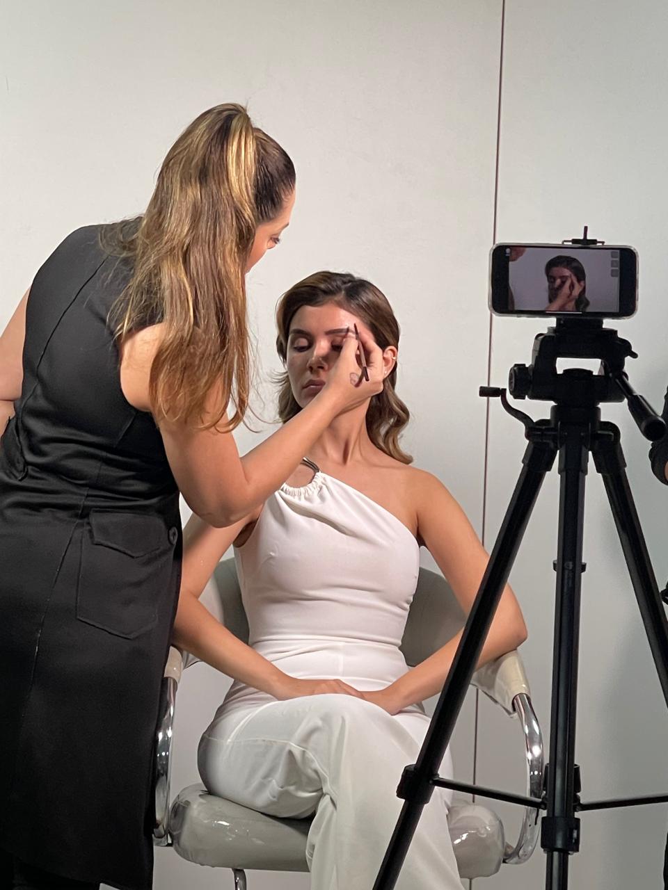 Maquiadora aplicando sombra em modelo durante demonstração gravada